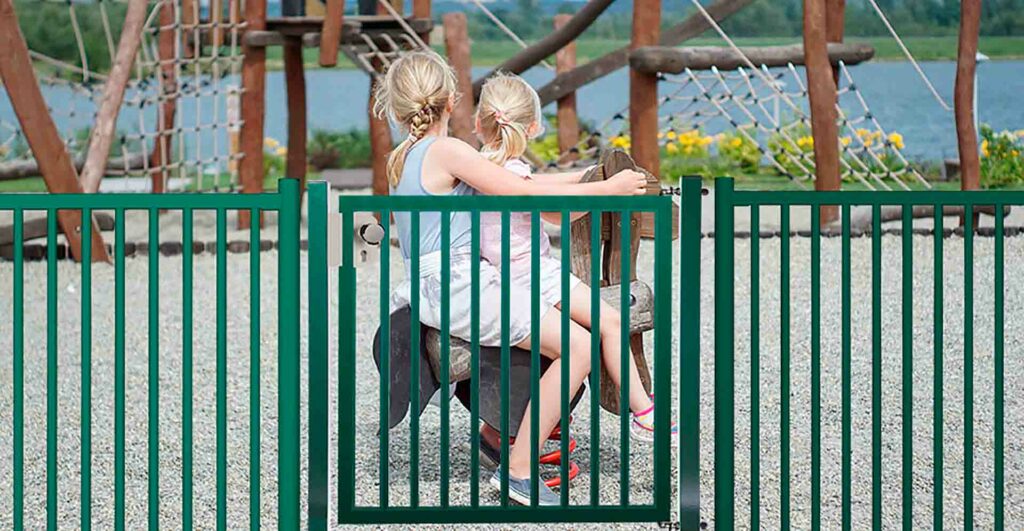 Puerta abatible Diabolo Plus de una hoja de color verde instalada en un parque infantil